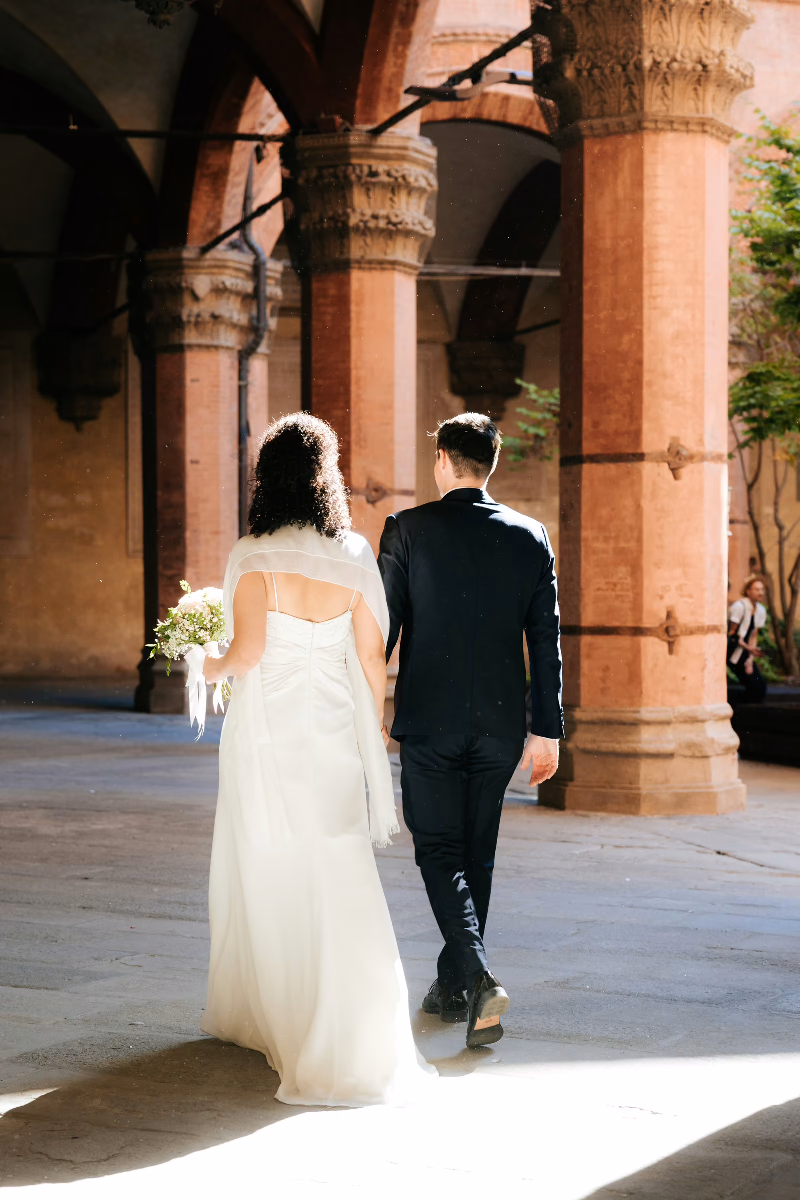 Kevin e Francesca camminano sotto un portico con colonne in mattoni