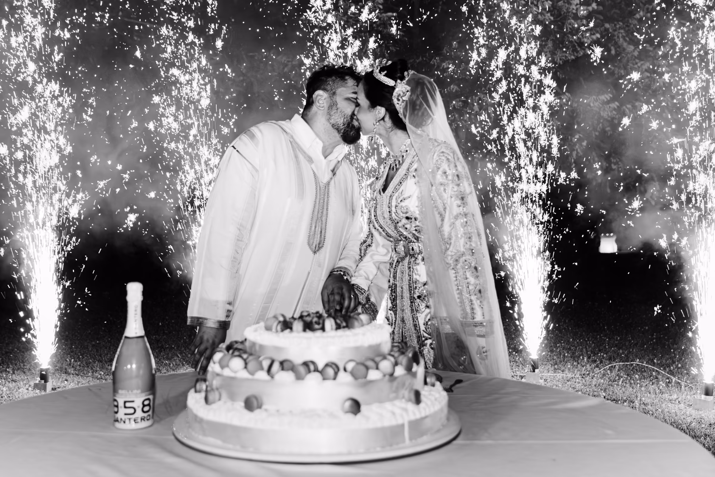 Sue e Leonardo si baciano dietro la torta, con fontane luminose ai lati, in bianco e nero